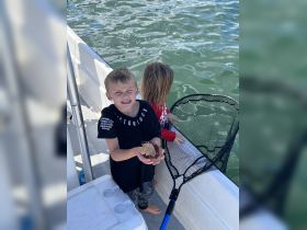 Two children enjoy a fun fishing experience on a boat, showcasing their catch while interacting with marine wildlife — a perfect family adventure on the water.