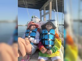 Two children enjoy a sunny day on a boat, wearing life jackets and smiling, capturing the joy of a family outing on the water.