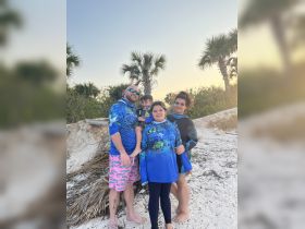 A joyful family poses together on the beach, dressed in vibrant matching outfits, capturing a memorable moment during their seaside adventure.