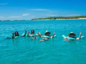A lively group enjoys a sunny day floating in crystal-clear waters, showcasing the perfect beach getaway experience.