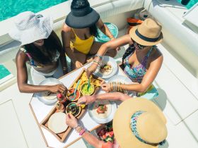 A vibrant group of friends enjoys a delicious meal aboard a boat, sharing tacos and dips while soaking up the sun — perfect for a fun day on the water.