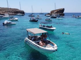 A vibrant scene of guests enjoying a sunny day on the water, with multiple boats anchored in crystal-clear turquoise waters — perfect for summer adventures and group outings.