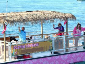 A cheerful group waves from a tiki boat, showcasing a fun and festive atmosphere on the water — perfect for private charters and celebrations.