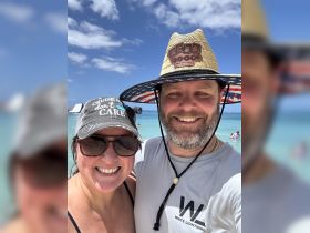 A cheerful couple poses for a selfie on the beach, showcasing their fun vacation vibes under the sun.