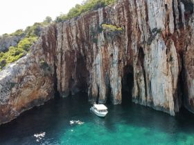 A stunning aerial view of a boat anchored near dramatic cliffs, with swimmers enjoying the crystal-clear waters — a perfect spot for exploration and adventure.