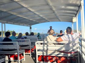 Guests seated inside a boat listen to a guide, showcasing the comfortable interior setup perfect for informative tours on the water.