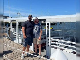 Two friends pose together at the boat dock, ready for a day of adventure on the water, with a jet ski in the background.