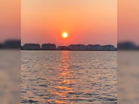 A stunning sunset casts a warm glow over the water, with reflections shimmering on the surface — a perfect backdrop for evening boat rides.