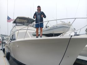 A man gives a thumbs up while standing on the bow of a boat at the marina, showcasing a perfect day for boating adventures.