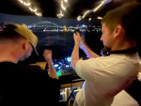 Two DJs perform on a boat at night, with the iconic Sydney Harbour Bridge illuminated in the background — a vibrant scene capturing the essence of nightlife on the water.