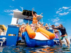 A lively group enjoys a fun-filled day on the water, with friends jumping off a water slide into the sea — perfect for summer parties and aquatic adventures.