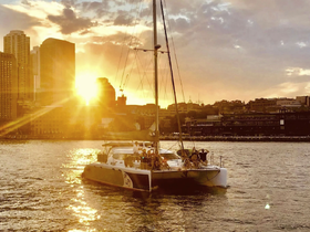 A vibrant sunset casts a golden glow over a catamaran with guests enjoying the view against a stunning city skyline — perfect for memorable evening cruises.