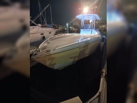 A sleek speedboat docked at night, illuminated by onboard lights, showcasing its design and structure against a backdrop of other vessels.