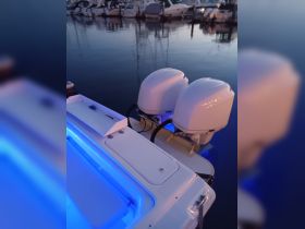 A close-up view of the back of a boat featuring dual outboard motors, illuminated by blue lighting, docked in a marina setting.