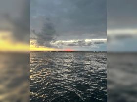 A stunning sunset over the water, showcasing the beautiful coastline and dramatic clouds — perfect for capturing the essence of a serene evening on the water.