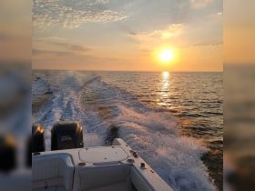A stunning sunset view from the back of a boat, showcasing the tranquil waters and the boat's wake as it cruises along the horizon.