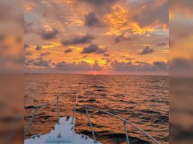A stunning sunset view from the bow of a boat, showcasing vibrant colors reflecting on the water — perfect for serene evening cruises.