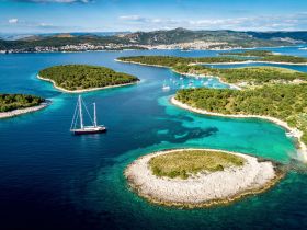 A stunning aerial view of a sailboat navigating through crystal-clear waters, surrounded by lush green islands — an ideal scene for sailing enthusiasts and nature lovers.