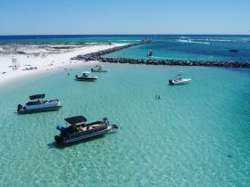 A vibrant scene at a sandy beach with multiple boats anchored in clear waters, showcasing a perfect day for swimming and relaxation.