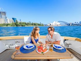 A couple enjoys a romantic dining experience on a boat with stunning views of Sydney's iconic landmarks, perfect for special occasions or sunset cruises.