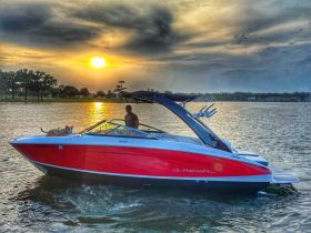 A man enjoys a sunset cruise on a Regal boat with his dog, capturing a serene moment on the water as the sun sets in the background.