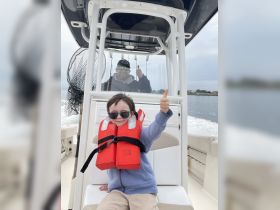 A joyful moment aboard a boat as a child and an adult give thumbs up, showcasing family fun and safety with life jackets.