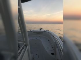 A serene view of the interior of a boat, showcasing the helm and seating area against a backdrop of a colorful sunset over calm waters.