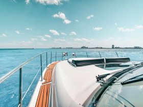 A stunning view from the bow of a yacht cruising through crystal-clear waters, showcasing the beautiful horizon and a glimpse of the city skyline.