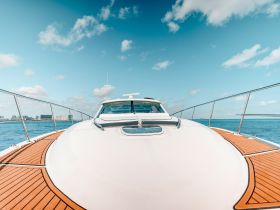 A stunning view of the front of a yacht cruising through clear waters, showcasing its sleek design and beautiful wooden deck.