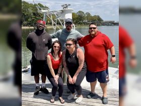 A cheerful group of friends poses together on the dock with a boat in the background, capturing a memorable moment during their boating adventure.