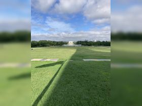 A wide shot of a grassy area with a distant monument under a cloudy sky. The image lacks clarity and focus.