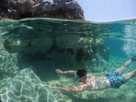 A swimmer explores the vibrant underwater world while snorkeling near rocky formations, showcasing the beauty of marine life and crystal-clear waters.