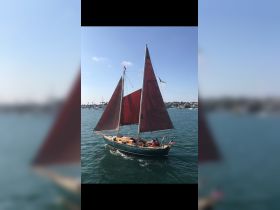 A beautiful sailing vessel with red sails glides through the water, showcasing a group of people enjoying their time on board — perfect for sailing adventures.