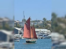 A beautiful sailing vessel with red sails navigates through a vibrant harbor, showcasing the joy of sailing and coastal adventures.