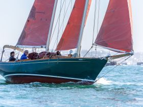 A sailing boat glides through the water with two crew members on board, showcasing the thrill of sailing adventures.