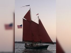 A beautiful sailing vessel with striking red sails glides through the water at sunset, creating a picturesque scene perfect for evening cruises.