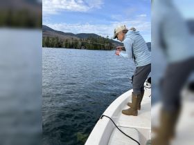 A woman enjoys fishing from a boat, showcasing the thrill of on-water activities amidst a scenic backdrop of mountains and trees.