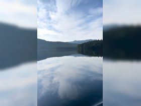 A tranquil scene of a lake reflecting the sky and surrounding mountains, creating a serene atmosphere.