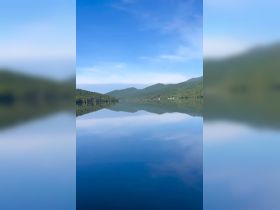 A serene view of a tranquil lake surrounded by lush mountains, reflecting the clear blue sky — an ideal backdrop for peaceful boating adventures.