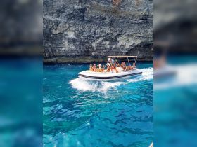 A lively group enjoys a fun day on the water aboard a speedboat, surrounded by stunning turquoise waters and rocky cliffs — perfect for adventure and exploration.