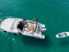 Aerial view of a sleek boat with a person at the helm, navigating through clear turquoise waters — perfect for exploring coastal destinations.