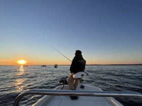 A serene sunset fishing experience on the water, showcasing a lone angler casting a line as the sun dips below the horizon.