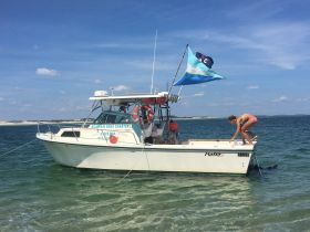 A woman prepares to jump off the bow of a boat anchored in shallow waters, showcasing a fun beach day perfect for water activities and charters.