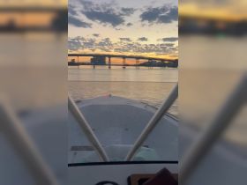 A serene sunset view from the bow of a boat, showcasing a bridge and calm waters — perfect for evening cruises and scenic adventures.
