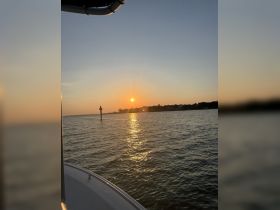 A serene sunset view from the deck of a boat, showcasing the tranquil waters and a distant shoreline — perfect for evening cruises.
