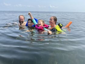 A joyful family enjoys a fun day swimming in the ocean, with children showcasing their excitement and colorful floatation devices — a perfect moment for summer adventures.