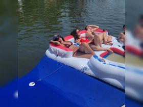A group of friends relaxes on a colorful floating mat in the water, enjoying a sunny day — perfect for summer fun and relaxation.