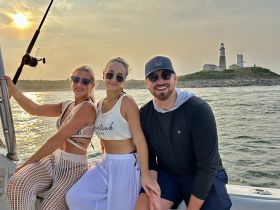 A group of friends enjoys a beautiful sunset on the water, with a lighthouse in the background, capturing the essence of a perfect boating adventure.