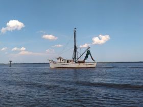 A classic fishing boat, the 'Stormy Seas,' navigates calm waters under a clear blue sky, showcasing its sturdy design and functionality.