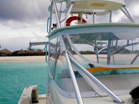A close-up view of a boat's helm with a scenic beach in the background, showcasing the vessel's design and the tranquil turquoise waters.